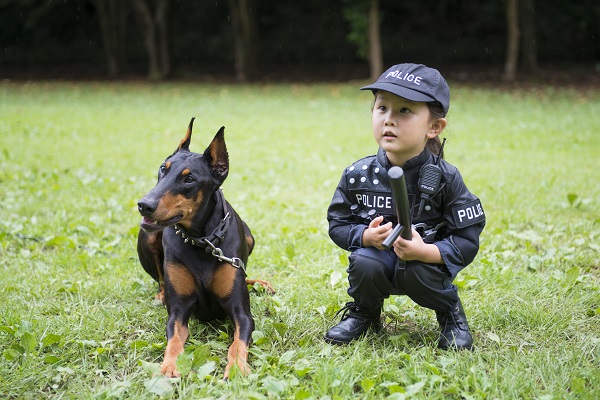 Dobermann ao lado de uma menina com roupa policial