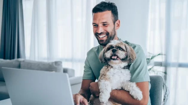 Petlovo - homem segurando seu cachorro no colo, enquanto utiliza o computador para compras online na pet friday da Petlove