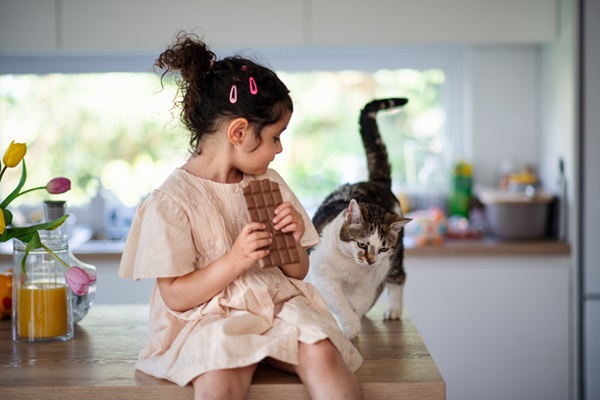 ato na cozinha ao lado de menina que segura uma barra de chocolate. 