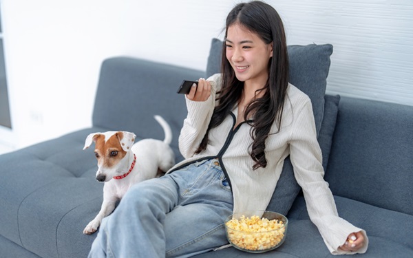 Mulher assistindo filme com cachorro no sofá.